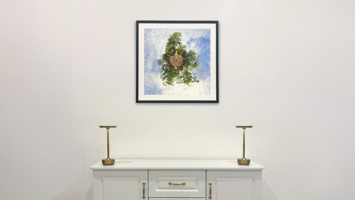 Framed Little Big World fine art print displayed in a minimalist interior above a white cabinet with gold lamps.